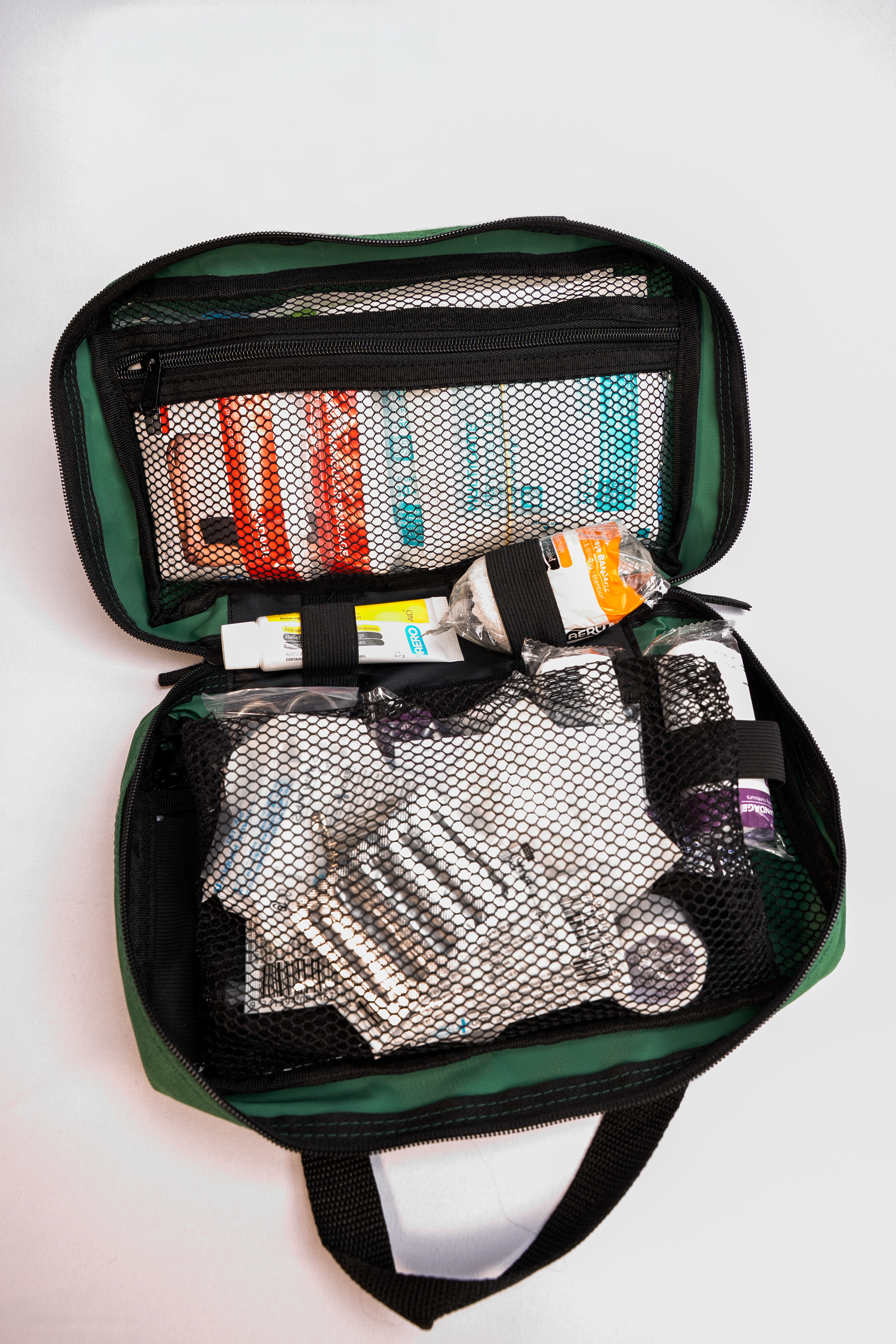 Open green first aid kit with fist aid supplies on a white background