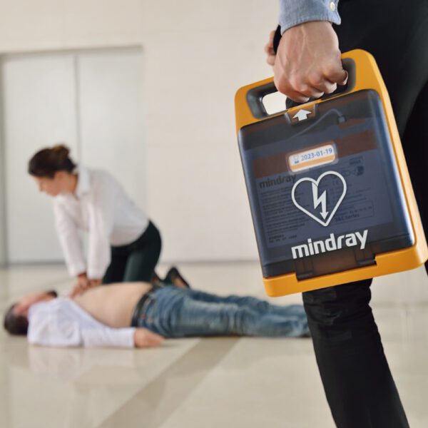 Person holding a Mindray defibrillator in a training scenario with another person on the floor.